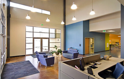 Well painted and coated floor and wall of an industrial painting supplies office with front desk, chairs, personal computer, floor mats, glass doors and windows, and lights hanged on the ceiling.